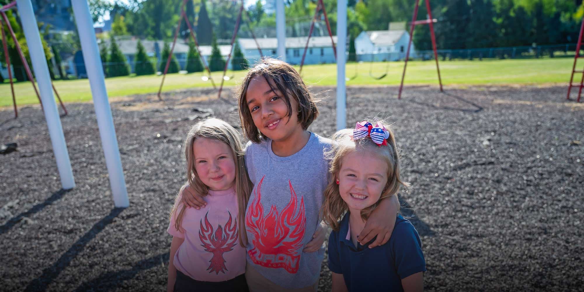 Three smiling students standing together on the school playground.