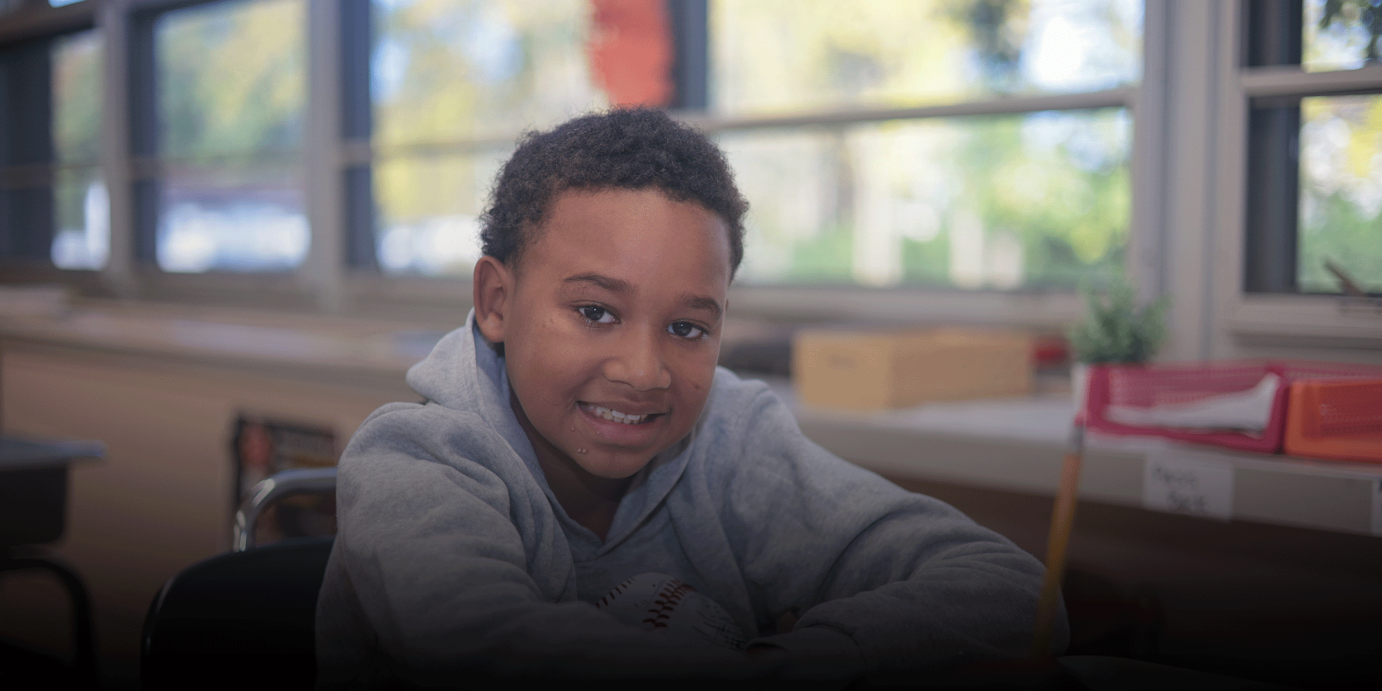 Smiling student sitting at a desk in a bright classroom.